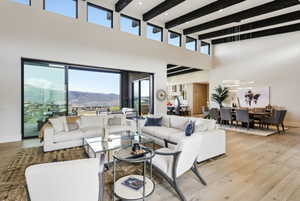 Spacious open-concept living area featuring a vaulted ceiling with exposed beams, large format light wood-finish flooring, and expansive sliding glass doors