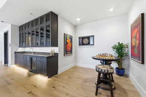 Indoor wet bar with glass insert cabinets, light wood-style flooring, dark stone counters, wine cooler, and recessed lighting