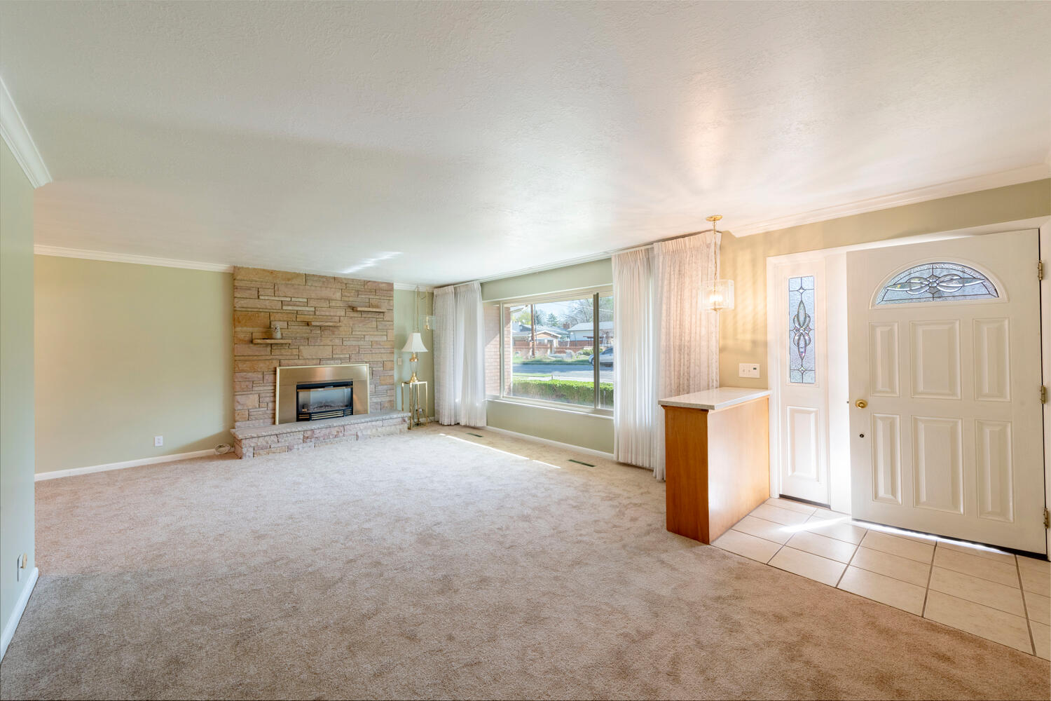 Entrance foyer featuring crown molding, light carpet, a stone fireplace, and light tile patterned flooring