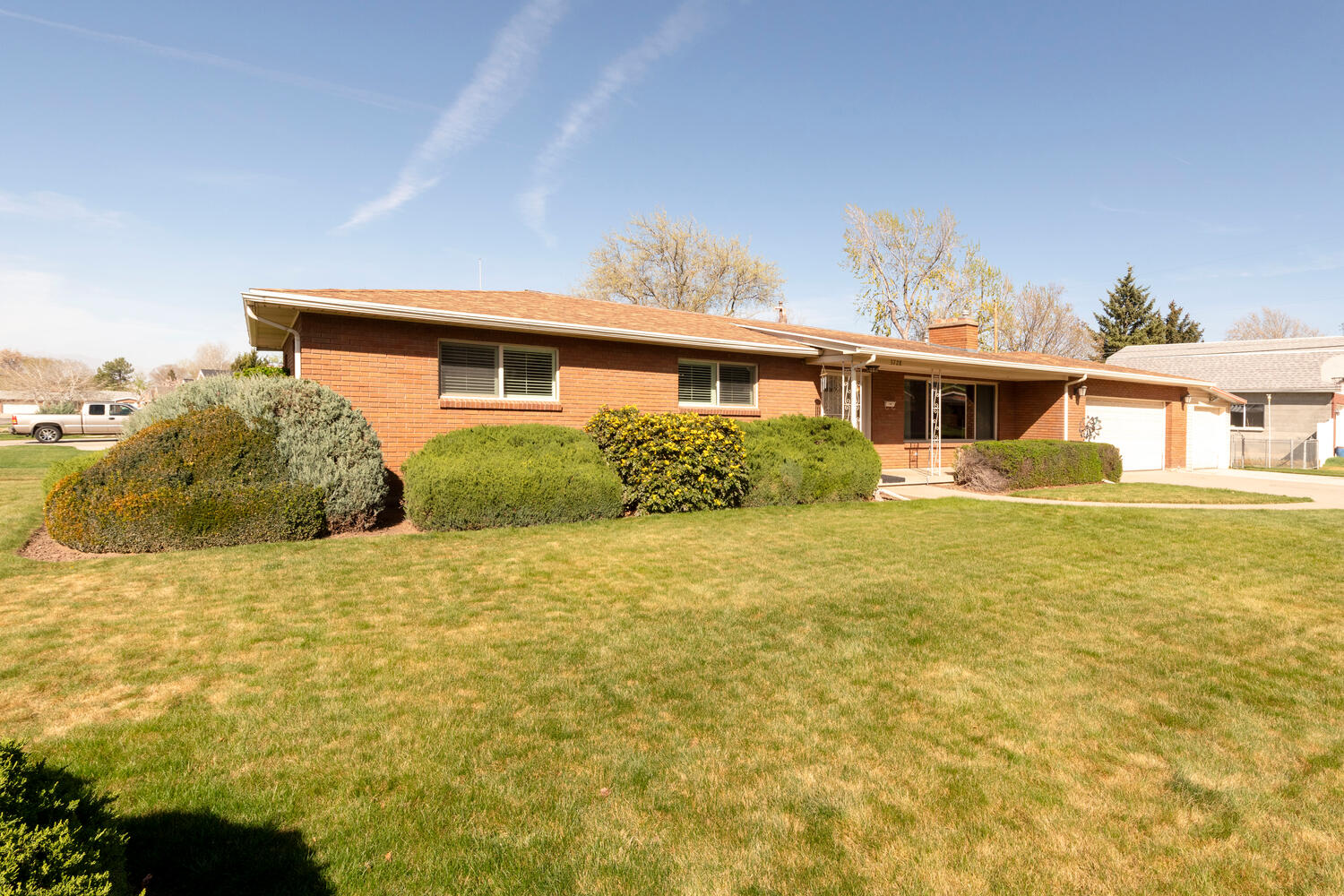 Ranch-style house featuring brick siding, a front lawn, a garage, a chimney, and covered porch