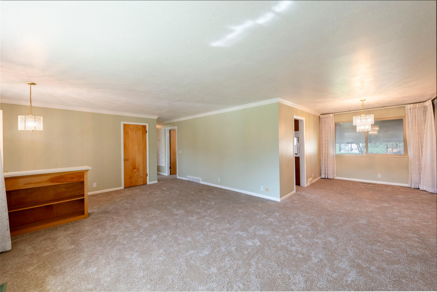 Empty room with hanging lights, light colored carpet, and ornamental molding