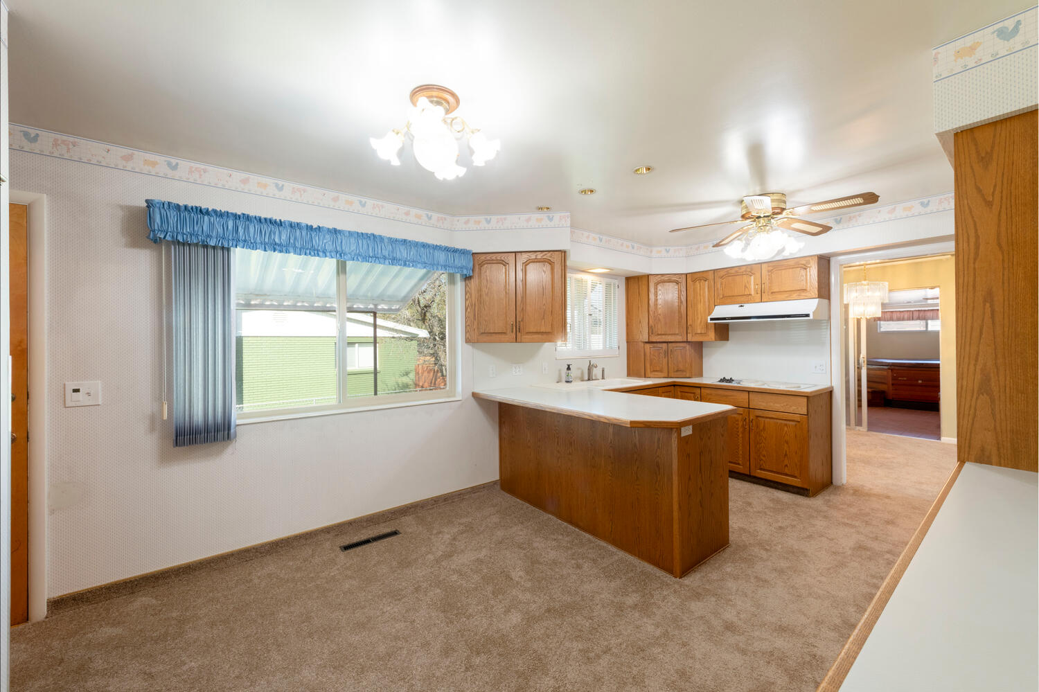 Kitchen with light countertops, a peninsula, light carpet, and wood finish cabinetry