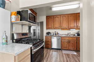 Kitchen with stainless steel appliances, wood finish cabinets, and dark wood-style flooring