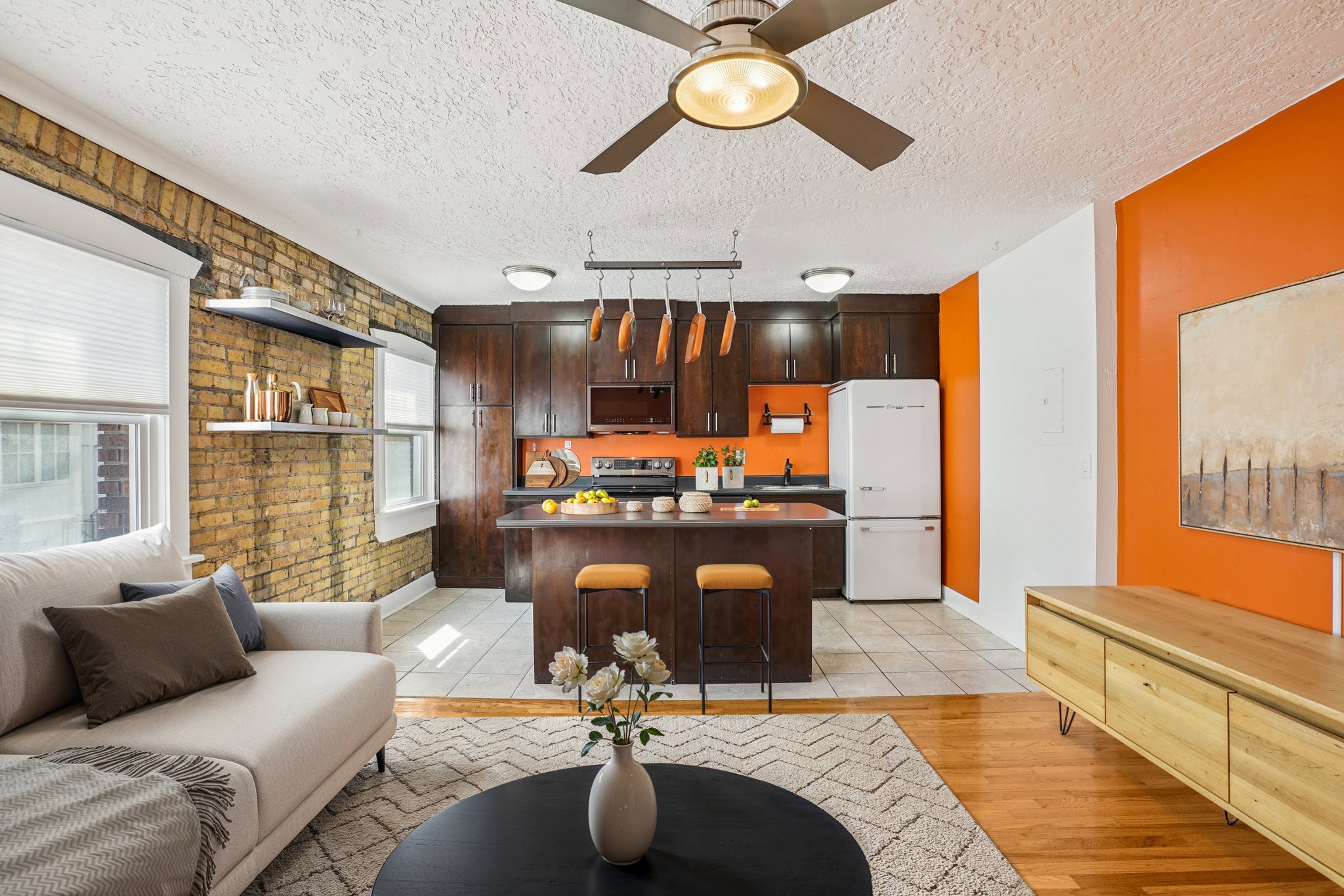 Living area featuring a ceiling fan, brick wall, a textured ceiling, and light wood-type flooring