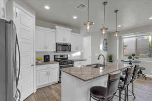 Kitchen with stainless steel appliances, a kitchen island with sink, white cabinets, and light wood finished floors