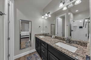 Ensuite bathroom featuring double vanity, a stall shower, and light wood-style floors