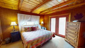 Bedroom featuring french doors, light colored carpet, wooden walls, and a wood ceiling with exposed beams
