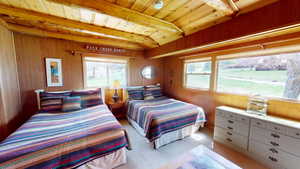 Bedroom with a wooden ceiling with exposed beams, wooden walls, and light colored carpet