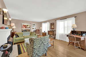 Living room with a gas log fireplace, original wood wood floors, abundant light, and high ceilings