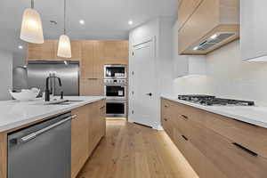 Kitchen with modern cabinets, built in appliances, light wood-type flooring, light stone counters, and decorative light fixtures