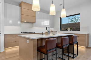 Kitchen with dual tone cabinets, an island with sink, a kitchen bar, decorative backsplash, and decorative light fixtures