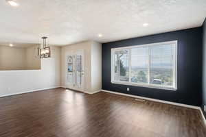 Unfurnished room with dark wood finished floors, a textured ceiling, and hanging lights