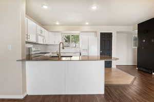Kitchen with dark stone counters, white appliances, dark wood-style floors, a peninsula, and white cabinetry