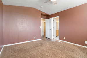 Unfurnished bedroom featuring lofted ceiling, light colored carpet, connected bathroom, and ceiling fan