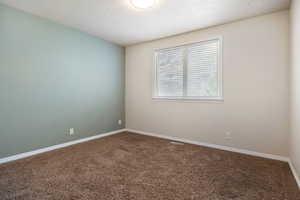 Spare room featuring dark colored carpet and a textured ceiling