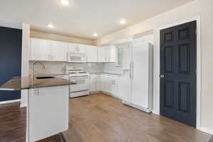 Kitchen featuring a kitchen breakfast bar, white appliances, a peninsula, white cabinetry, and recessed lighting