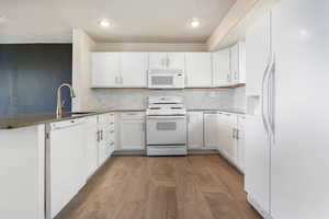 Kitchen featuring white appliances, white cabinetry, tasteful backsplash, a peninsula, and recessed lighting