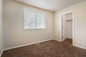 Unfurnished bedroom with a walk in closet, dark carpet, and a textured ceiling