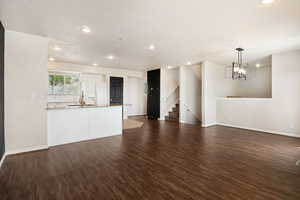 Unfurnished living room with dark wood finished floors and hanging lights