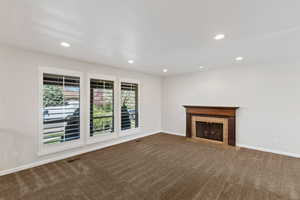 Unfurnished living room featuring dark carpet, recessed lighting, and a fireplace