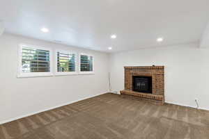 Unfurnished living room featuring dark carpet, recessed lighting, and a brick fireplace