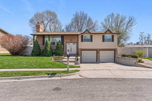 Bi-level home featuring brick siding, a garage, driveway, a chimney, and a gate