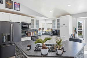 Kitchen with black appliances, a kitchen island, decorative backsplash, lofted ceiling, and glass fronted cabinets