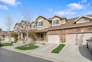 View of front of property featuring stone siding, covered porch, concrete driveway, stucco siding, and roof with shingles
