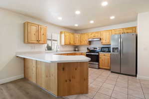 Kitchen featuring a peninsula, light countertops, stainless steel appliances, light wood finish cabinetry, and recessed lighting