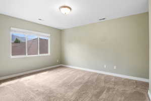Spacious room featuring neutral wall tones, plush carpeting, a large multi-pane window, white baseboards, and an overhead flush-mount light fixture