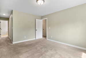 Spacious room featuring neutral carpeting, light-colored walls, white trim, a flush mount ceiling light, and white doors with dark hardware