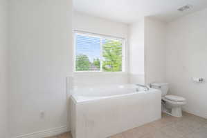 Soaking tub with white surround, set beneath a window with blinds