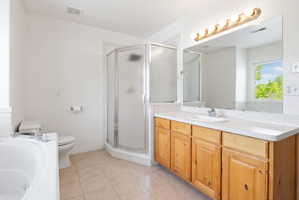 Bathroom featuring a built-in tub, separate glass-enclosed shower, wood-finish vanity with an integrated sink, broad wall-mounted mirror, and tile flooring
