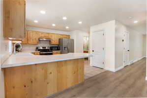 Kitchen featuring light wood-style flooring, stainless steel appliances, light countertops, a peninsula, and light wood finish cabinetry