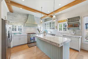Kitchen featuring marble backsplash, stainless steel appliances, marble countertops, a center island, white cabinetry, and custom range hood