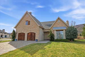 View of front facade featuring a front yard, a chimney, decorative driveway, and stone siding