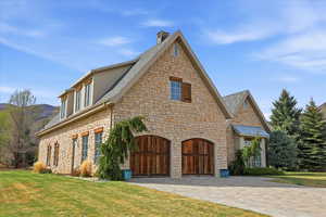 View of side of property featuring stone siding, driveway, a lawn, and a garage