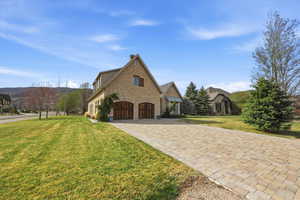 View of property exterior with stone siding, decorative driveway, a chimney, a lawn, and a garage