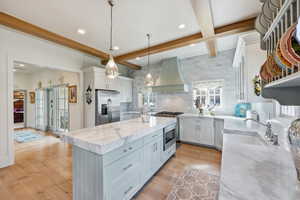 Dual tone kitchen with backsplash, marble counters, a kitchen island, beamed ceiling, and stainless steel appliances