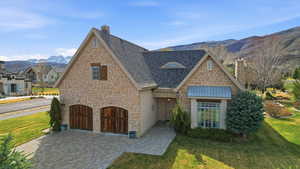 View of front facade with a mountain view, stone siding, a front lawn, and a chimney