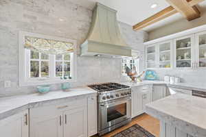 Kitchen with stainless steel gas range, glass fronted cabinets, , beam ceiling, and  marble counters