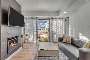 Living room with a textured ceiling, light wood-type flooring, and a warm lit fireplace