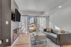 Living area with light wood-type flooring, a textured ceiling, and a glass covered fireplace