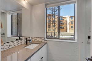Bathroom featuring a textured wall, vanity, and decorative backsplash