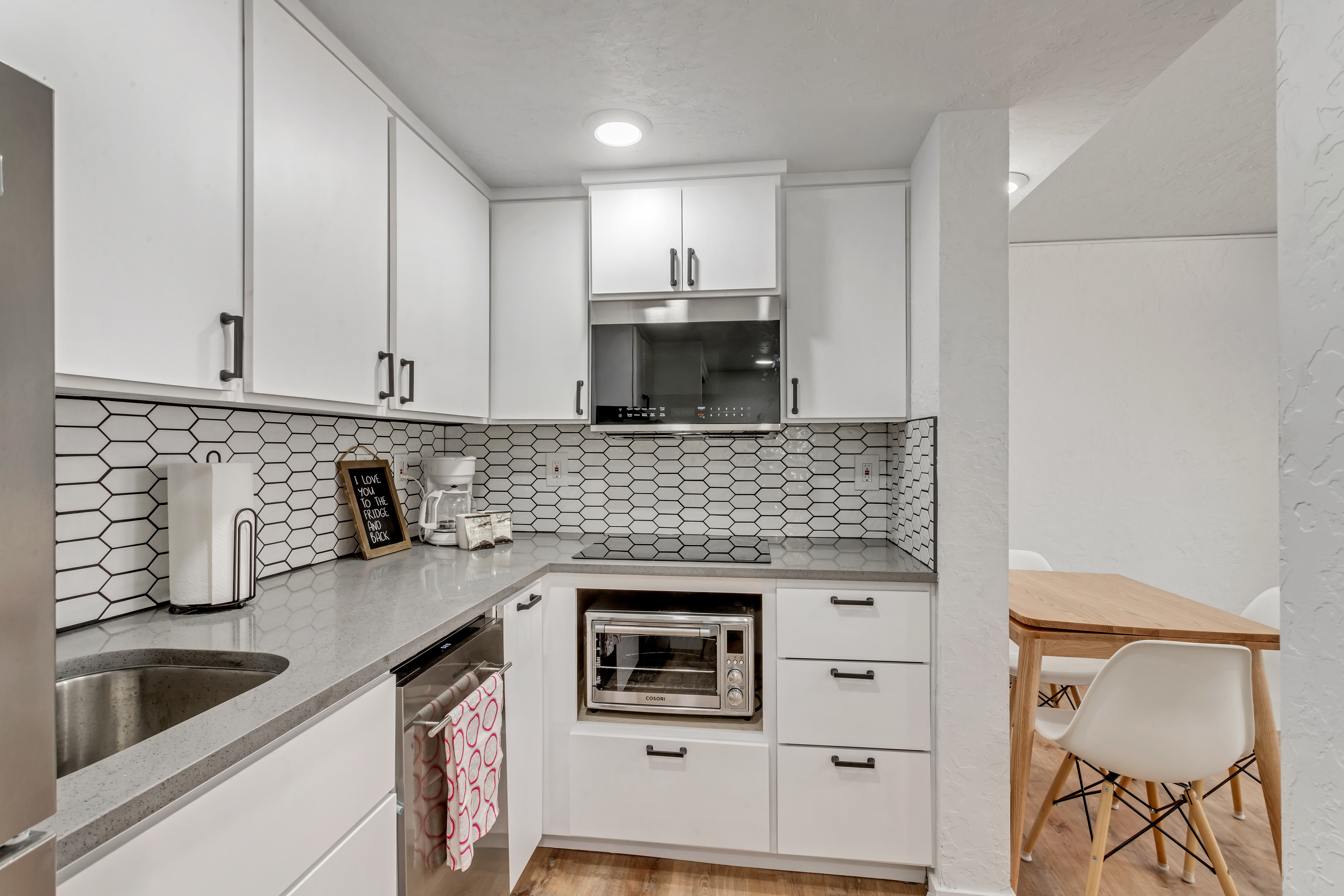 Kitchen featuring light stone counters, white cabinets, stainless steel appliances, light wood-style floors, and decorative backsplash