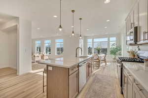 Kitchen featuring stainless steel appliances, light wood finished floors, light stone counters, a kitchen island with sink, and open floor plan