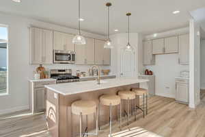 Kitchen featuring stainless steel appliances, light wood-style floors, an island with sink, a kitchen breakfast bar, and hanging light fixtures