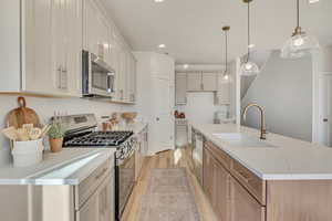 Kitchen featuring stainless steel appliances, a center island with sink, light wood-style floors, pendant lighting, and light stone countertops