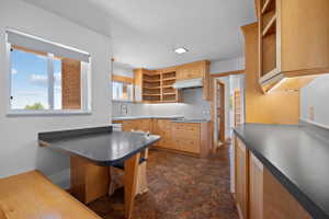 Kitchen featuring light wood cabinetry, dark countertops, built-in dining table with bench seating, under-cabinet lighting, and patterned flooring