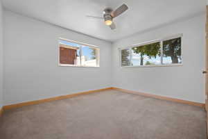 Carpeted room with a ceiling fan light fixture, two windows, and light wood-finish baseboards